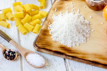 White dry rice over kitchen board with some vegetables and pasta around.