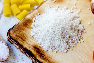 White dry rice over kitchen board with some vegetables and pasta around.
