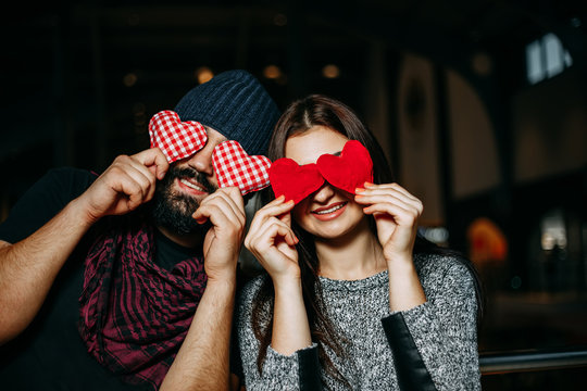 Happy young couple covering eyes with red pillow hearts and smil