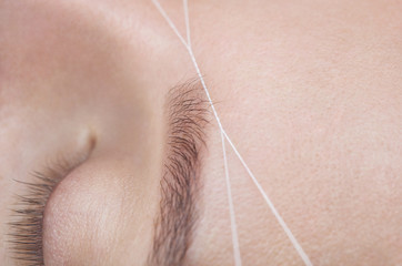 The make-up artist plucks her eyebrows with a thread close-up. Face care beauty treatments in the beauty salon.