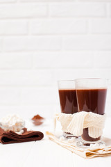 Warm cocoa in glasses with marshmallow, crocahet decorations, brown and beige napkins on white wooden background. Hot chocolate. Sweet drink. Close up photography. Vertical banner