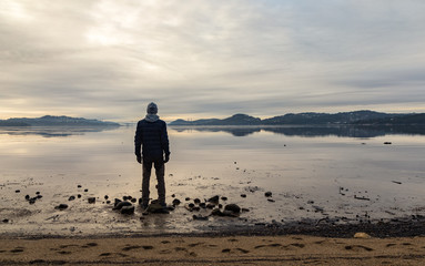 Man standing at the beach, looking at the calm sea and the mist and fog. Hamresanden, Kristiansand, Norway