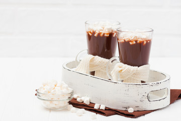 Warm cocoa in glasses with marshmallow, crocahet decorations, brown and beige napkins on white wooden background. Hot chocolate. Sweet drink. Close up photography. Hoizontal banner