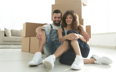 married couple sitting near cardboard boxes in a new apartment