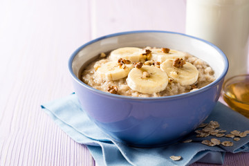 Oatmeal porridge with banana, walnuts and honey in bowl on purple wooden background. Healthy breakfast.
