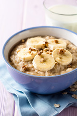 Oatmeal porridge with banana, walnuts and honey in bowl on purple wooden background. Healthy breakfast.