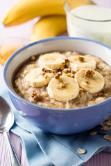 Naklejka na ściany i meble Oatmeal porridge with banana, walnuts and honey in bowl on purple wooden background. Healthy breakfast.