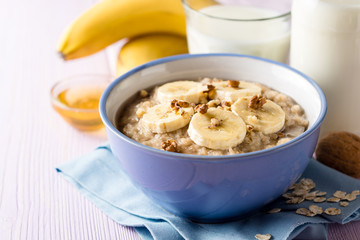 Oatmeal porridge with banana, walnuts and honey in bowl on purple wooden background. Healthy breakfast.