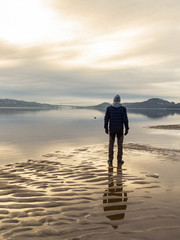 Man standing at the beach, reflections of the man in the water. Calm sea, mist and fog. Hamresanden, Kristiansand, Norway