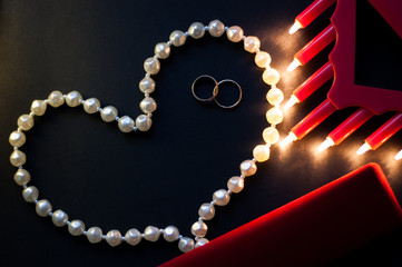 wedding rings, a string of pearls on a black background, burning lights, a red box. St. Valentine's...