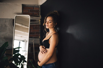Fototapeta na wymiar Happy beautiful pregnant caucasian woman with big belly in black underwear sits on the bed in the bedroom, future parrents, waiting for a child, motherhood