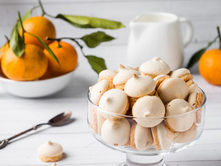 Cookies meringue in a glass vase mandarins with green leaves in a plate on white background