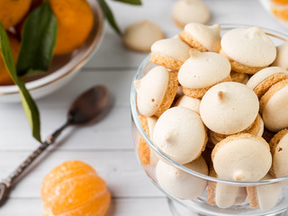 Cookies meringue in a glass vase mandarins with green leaves in a plate on white background