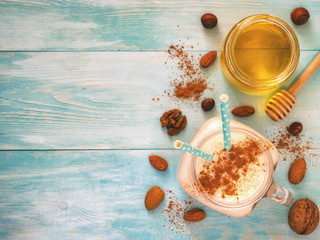 Banana smoothie decorated by cinnamon powder in mason jar on turquoise rustic wooden background with honey and nuts. Top view or flat lay. Copy space