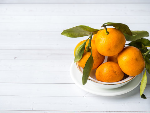 Fresh mandarin or tangerines with stems and leaves on the plate on white wooden background Copy space