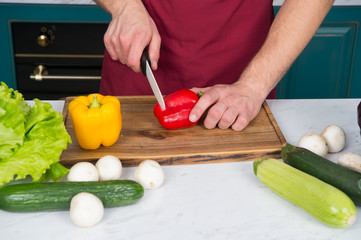 Hands cut red pepper with knife on wooden cutting board