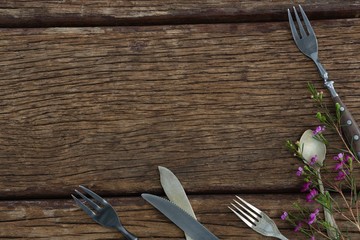 Fork, butter knife and spoon with flower on wooden table