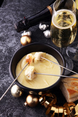 Gourmet Swiss fondue dinner on a winter evening alongside a heated pot of cheese fondue with two forks dipping bread and champagne