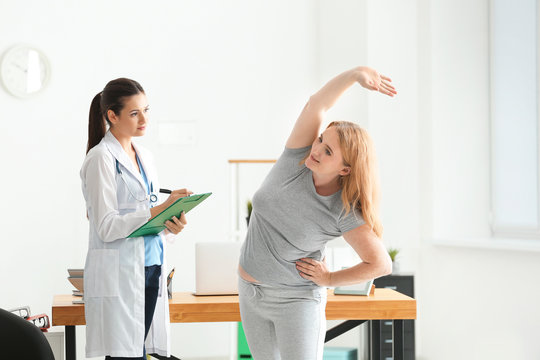 Young female doctor observing overweight woman during exercise in clinic
