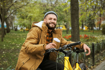 Fototapeta premium Attractive young hipster with cup of coffee and bicycle in park