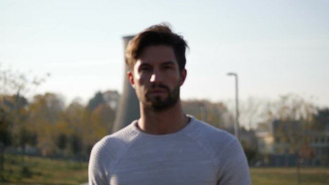 Sexy handsome young man in jeans and white sweater walking in city park