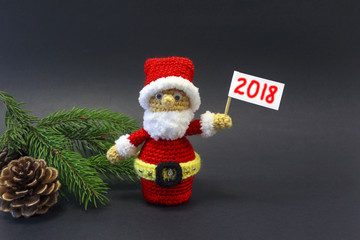  puppet Santa on a dark background among the branches of a Christmas tree with a poster 2018