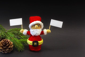  Santa doll on a dark background among the branches of a Christmas tree with tablets in hands