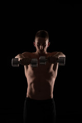 Young athlete exercise with hand weights on black background