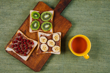 Fresh sandwiches for breakfast with bananas, kiwi and berries with cup of tea. Fruit mix.