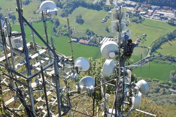 Antennen-Techniker bei der Reparatur hängt an einer Sendeanlage hoch über dem Abgrund (Lago...