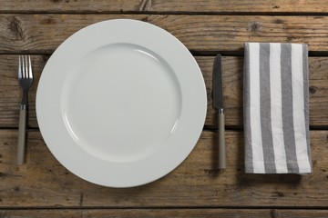 Plate with cutlery and napkin on wooden table