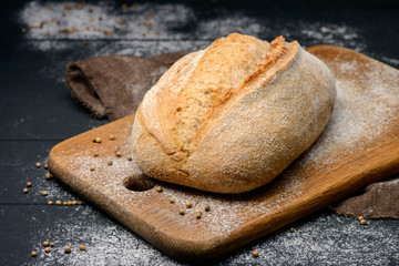 Close-up photo of bread on a wooden board with flour around on black background