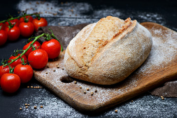 Composition of bread and sprigs of fresh tomatoes on a wooden board with flour around . Close-up photo