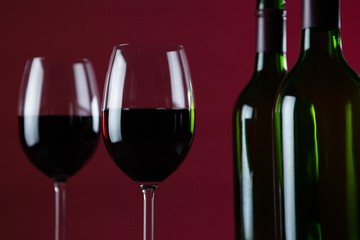 Wine glasses and bottles against red background