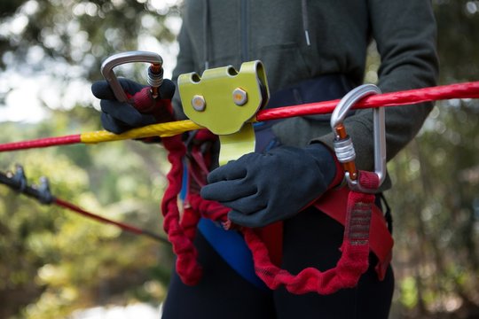Woman adjusting her harness on zip line cable in the forest on a