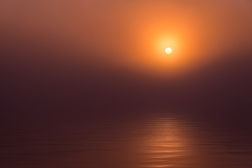 Red epic sunset over lake with reflection. Calm water and scenic sky merge together in mist.