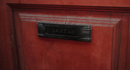 Cartas, caixa de correio antiga em metal fixada numa porta de madeira vermelha com inscrições em português