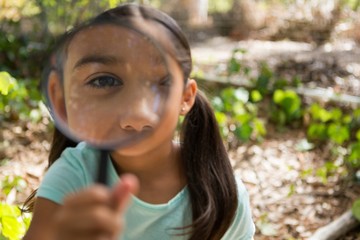 Little girl holding and looking through magnifying glass in the