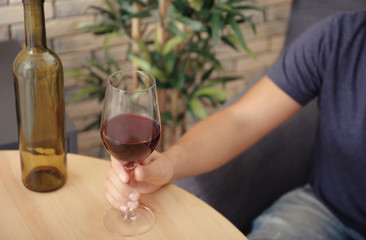 Man with glass of wine sitting at wooden table indoors. Alcohol dependence concept