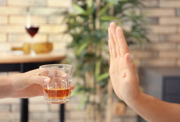 Hand of man refusing glass of alcohol indoors
