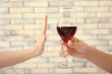 Hand of woman refusing glass of alcohol against brick wall