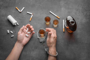 Man in handcuffs with cigarettes, drugs and alcohol at table. Concept of bad habits