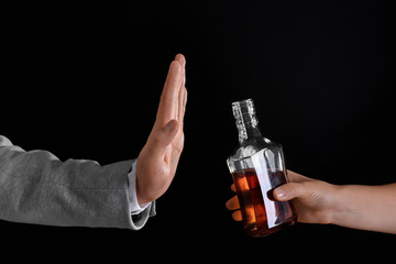 Hand of man rejecting bottle of alcohol against dark background