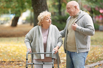 Elderly man and his wife with walking frame in autumn park