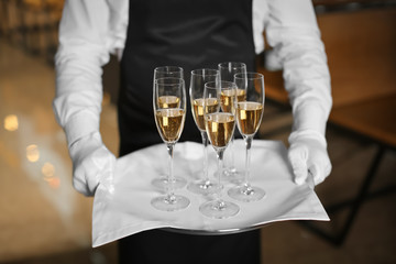Waiter holding tray with glasses of champagne indoors © Africa Studio