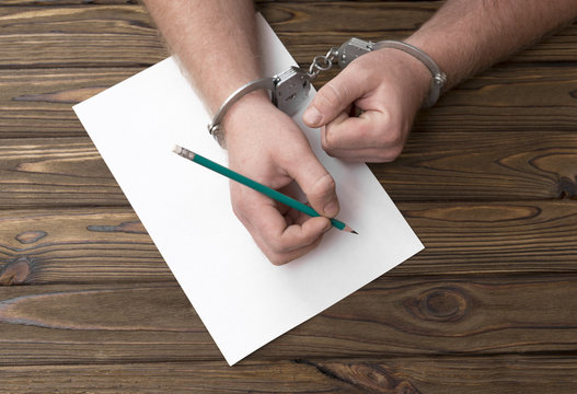handcuffs, pencil, paper on the background of a wooden table. confession
