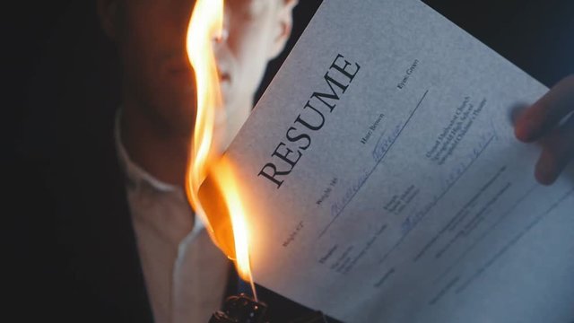 Close-up of businessman burns resume document in a dark background.