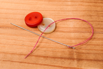 Cloth buttons and sewing needle with red thread on wooden table
