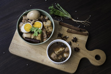 Eggs and sweet pork with fried tofu, boiled in brown sauce and in white bowl on old brown wooden plank (Thai food called 