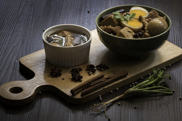 Eggs and sweet pork with fried tofu, boiled in brown sauce and in white bowl on old brown wooden plank (Thai food called 